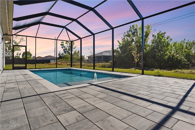 pool at dusk with a lanai, a patio area, and pool water feature