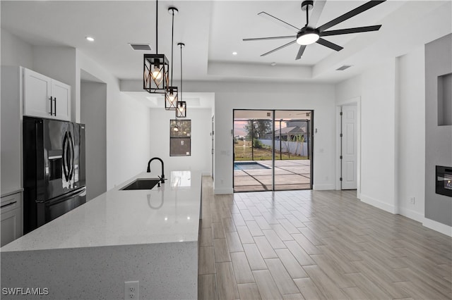 kitchen featuring hanging light fixtures, light hardwood / wood-style flooring, ceiling fan, refrigerator with ice dispenser, and light stone counters