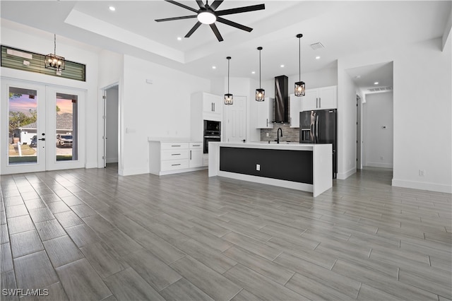 living room with ceiling fan with notable chandelier, light wood-type flooring, a tray ceiling, and sink