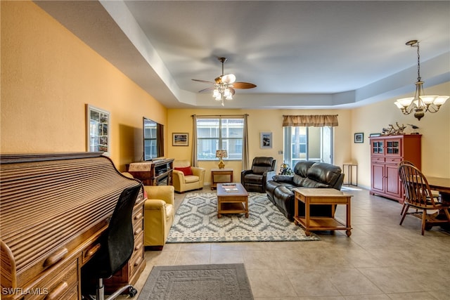 tiled living room featuring ceiling fan with notable chandelier and a raised ceiling