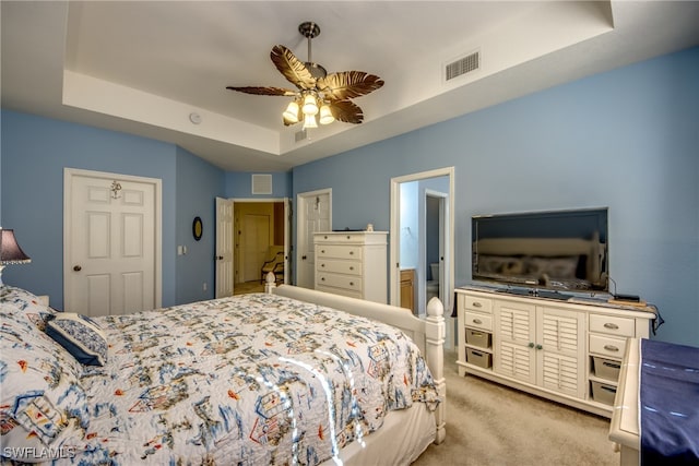 bedroom with ceiling fan, ensuite bathroom, light colored carpet, and a raised ceiling