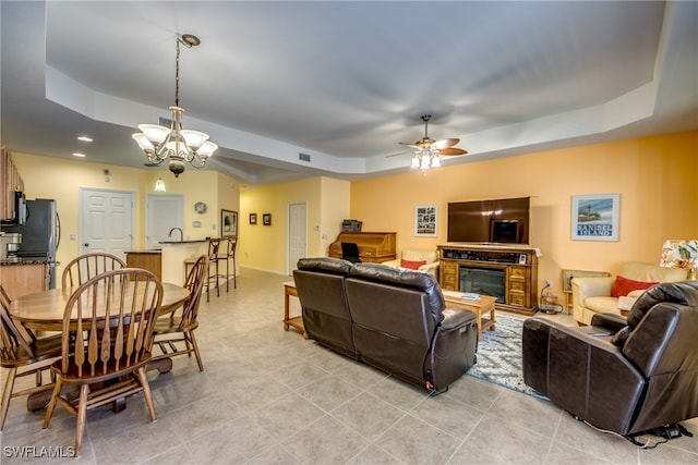 tiled living room featuring ceiling fan with notable chandelier and a raised ceiling