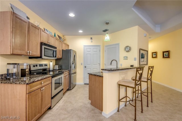 kitchen featuring light tile patterned floors, a kitchen bar, appliances with stainless steel finishes, decorative light fixtures, and dark stone countertops