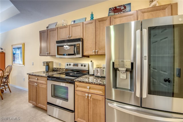 kitchen with light tile patterned flooring, stainless steel appliances, and dark stone countertops