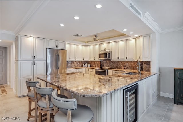 kitchen with stone counters, sink, beverage cooler, stainless steel appliances, and kitchen peninsula