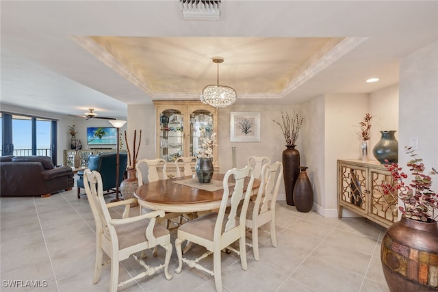 tiled dining area featuring a raised ceiling, ceiling fan with notable chandelier, and ornamental molding