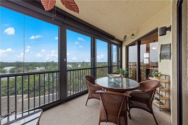 sunroom with ceiling fan and a water view