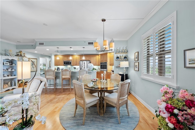 dining room with an inviting chandelier, crown molding, and light hardwood / wood-style flooring