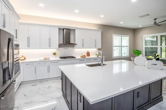 kitchen featuring wall chimney range hood, a center island with sink, white cabinetry, and stainless steel appliances