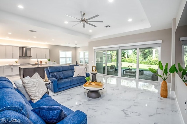 living room with a tray ceiling, ceiling fan, and a healthy amount of sunlight