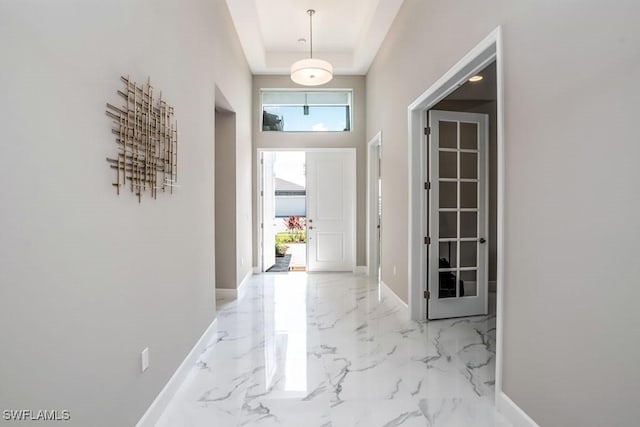 foyer entrance featuring a towering ceiling, marble finish floor, baseboards, and a raised ceiling