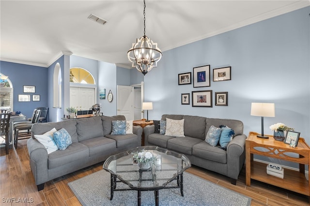 living room with ornamental molding, visible vents, an inviting chandelier, and wood finished floors