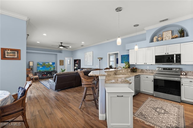 kitchen with appliances with stainless steel finishes, open floor plan, a peninsula, white cabinetry, and a sink