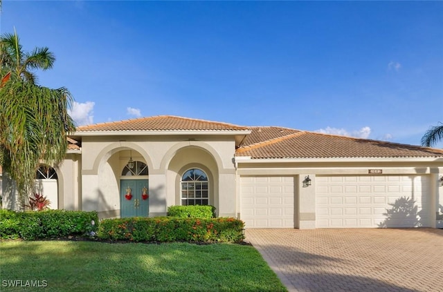 mediterranean / spanish-style house with decorative driveway, a tiled roof, an attached garage, and stucco siding