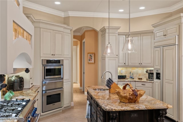 kitchen featuring decorative light fixtures, paneled built in fridge, light stone countertops, and an island with sink