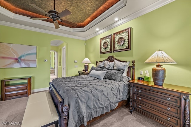 carpeted bedroom with a tray ceiling, ceiling fan, ornamental molding, and ensuite bathroom