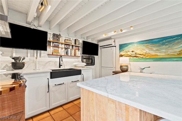 kitchen with sink, beamed ceiling, white fridge, light stone counters, and white cabinetry