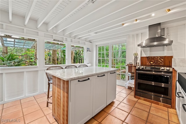 kitchen featuring a kitchen island, light stone counters, wall chimney range hood, and white cabinetry