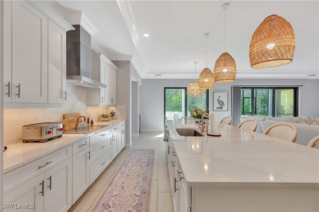 kitchen with a healthy amount of sunlight, wall chimney range hood, and a large island with sink