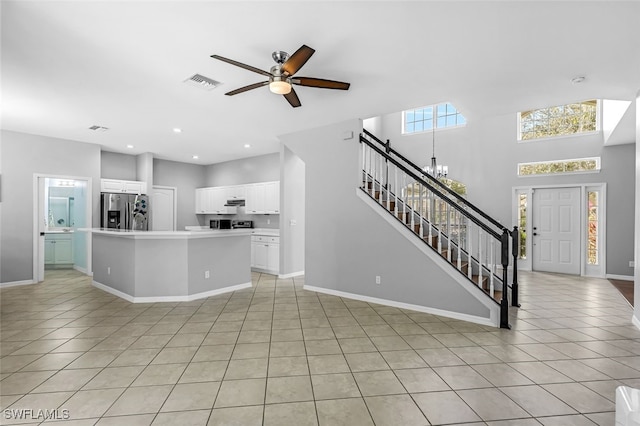 unfurnished living room featuring light tile patterned floors, a high ceiling, and ceiling fan with notable chandelier