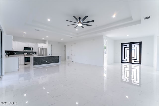 unfurnished living room featuring a raised ceiling, ceiling fan, and sink