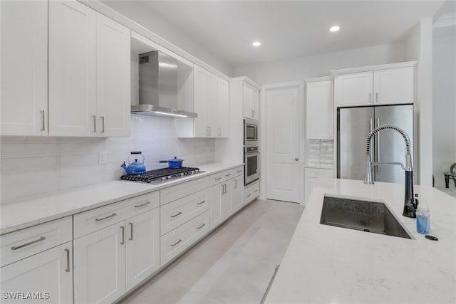 kitchen with backsplash, wall chimney exhaust hood, stainless steel appliances, sink, and white cabinetry