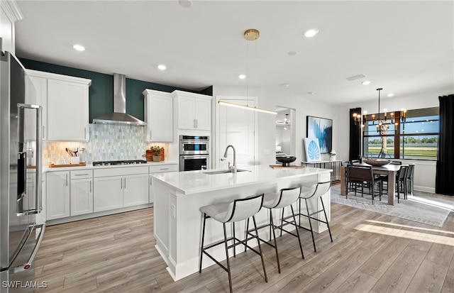 kitchen with white cabinetry, wall chimney range hood, sink, and stainless steel appliances