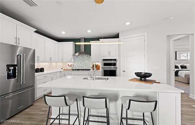 kitchen with white cabinets, a kitchen island with sink, wall chimney exhaust hood, and stainless steel appliances