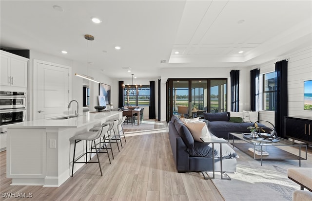 living room with light wood-type flooring, plenty of natural light, a notable chandelier, and sink