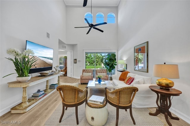 living room with ceiling fan, light hardwood / wood-style floors, and a high ceiling