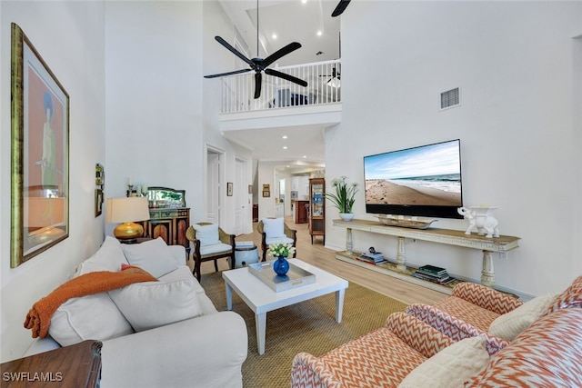 living room with ceiling fan, a towering ceiling, and wood-type flooring