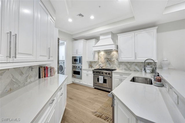 kitchen with white cabinetry, sink, premium range hood, appliances with stainless steel finishes, and light wood-type flooring