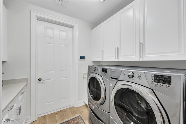 laundry room featuring cabinets, light hardwood / wood-style flooring, and washing machine and clothes dryer