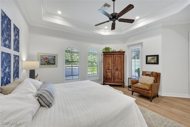 bedroom featuring a raised ceiling, multiple windows, ceiling fan, and light wood-type flooring