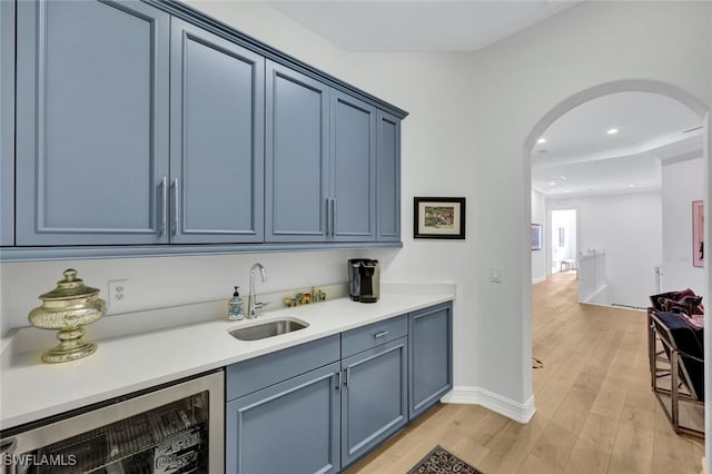 bar with blue cabinetry, sink, beverage cooler, and light hardwood / wood-style floors