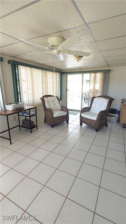 unfurnished living room featuring ceiling fan, a drop ceiling, and light tile patterned floors