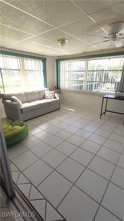 unfurnished living room with a drop ceiling, tile patterned flooring, and a ceiling fan