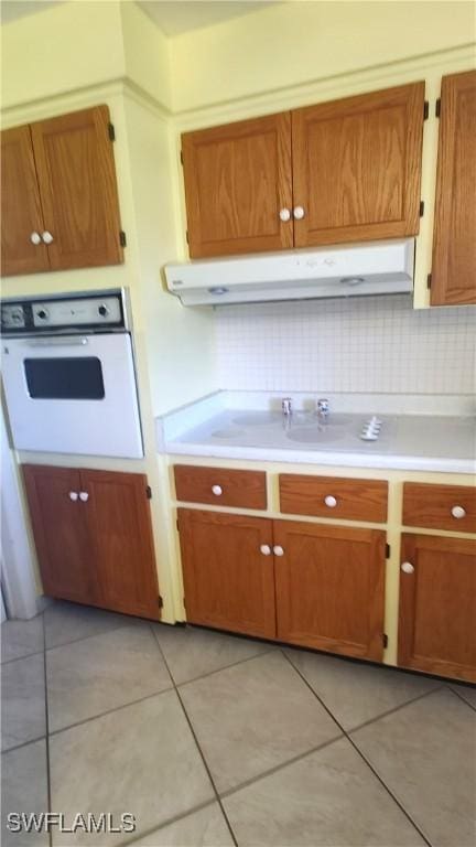 kitchen with light tile patterned floors, white oven, light countertops, under cabinet range hood, and backsplash