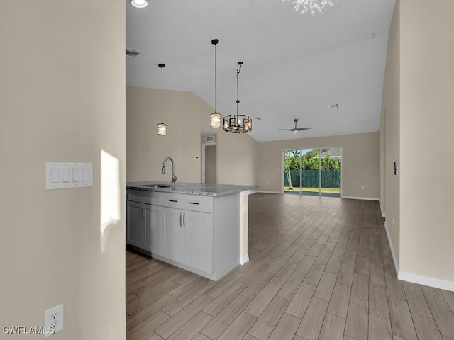 kitchen with ceiling fan with notable chandelier, sink, hanging light fixtures, light hardwood / wood-style flooring, and light stone countertops