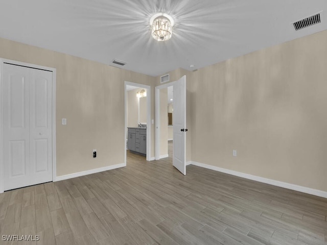 unfurnished bedroom featuring ensuite bathroom, an inviting chandelier, light wood-type flooring, and a closet