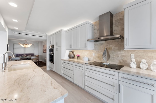 kitchen with sink, wall chimney exhaust hood, light wood-type flooring, tasteful backsplash, and light stone counters