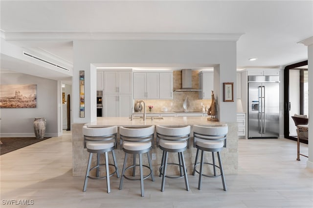 kitchen featuring light wood-type flooring, wall chimney exhaust hood, sink, white cabinetry, and built in fridge