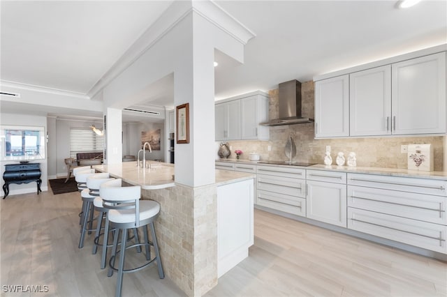 kitchen with light wood-type flooring, a center island with sink, wall chimney exhaust hood, and black electric cooktop