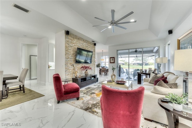 living area featuring a tray ceiling, visible vents, marble finish floor, and ceiling fan