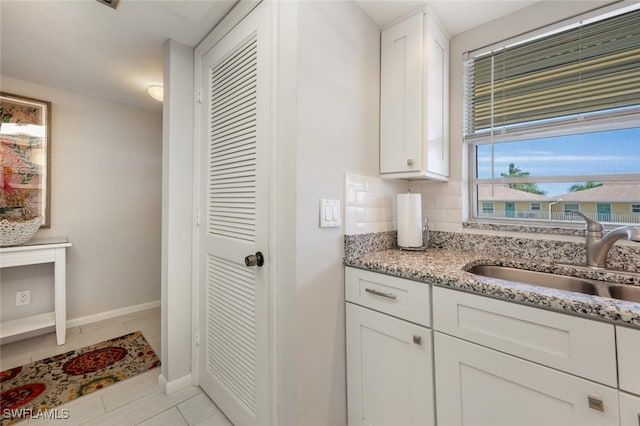 kitchen featuring sink, light tile patterned floors, light stone counters, decorative backsplash, and white cabinets