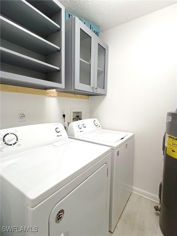 laundry area featuring cabinets, separate washer and dryer, water heater, and a textured ceiling