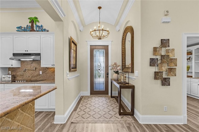 foyer entrance featuring a notable chandelier, light wood-type flooring, crown molding, and vaulted ceiling