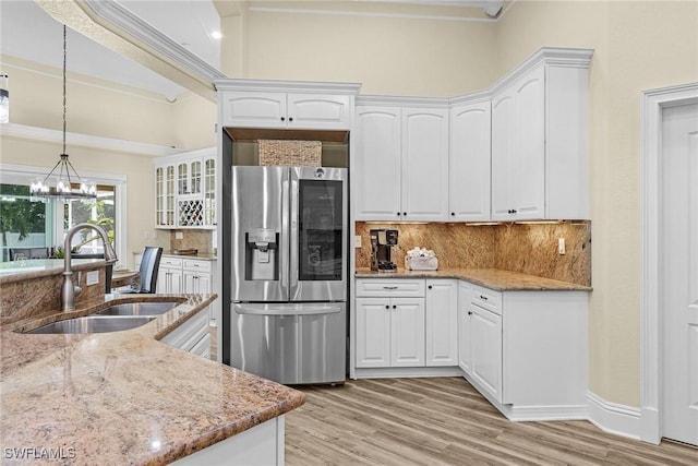 kitchen with light stone countertops, stainless steel fridge, sink, white cabinets, and light hardwood / wood-style floors