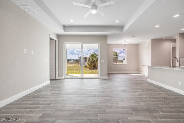 unfurnished living room with a ceiling fan, a raised ceiling, visible vents, and baseboards