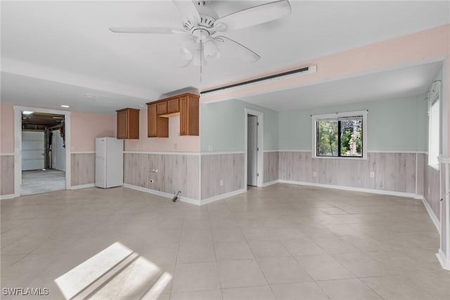 unfurnished living room with a ceiling fan, wainscoting, and wooden walls